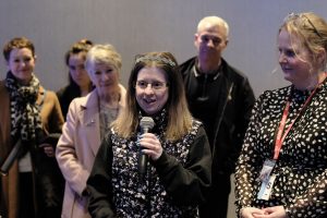 DanceSyndrome Founder Jen Blackwell speaking into a microphone at a DanceSyndrome event