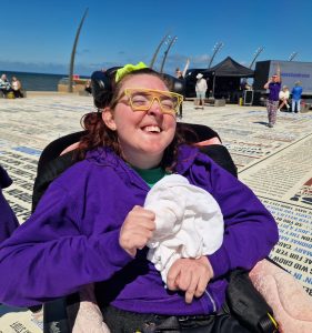 A photo of Jodie, a dancer who uses a wheelchair. She is dancing on the Comedy Carpet in Blackpool.