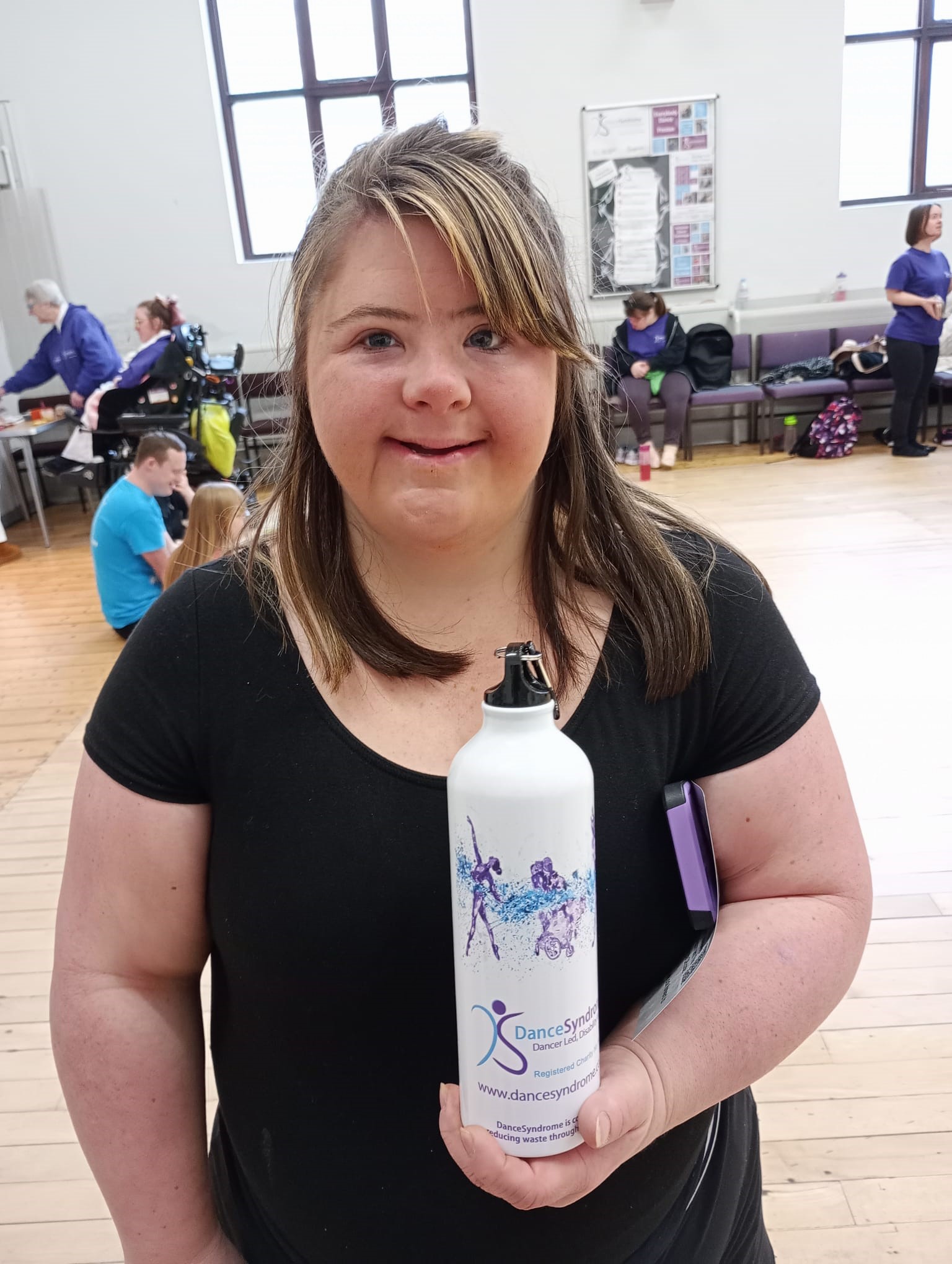 A picture of Lucy holding a reusable water bottle with a DanceSyndrome logo on.