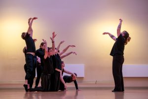 An iCreate rehearsal with a dancer raising their arms and a group of dancers reflecting the movement